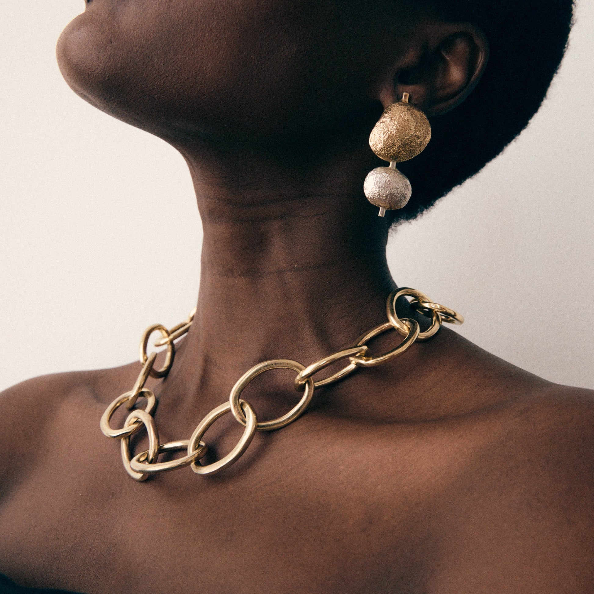 Close-up of a person wearing a gold chain necklace and earrings on a plain background
