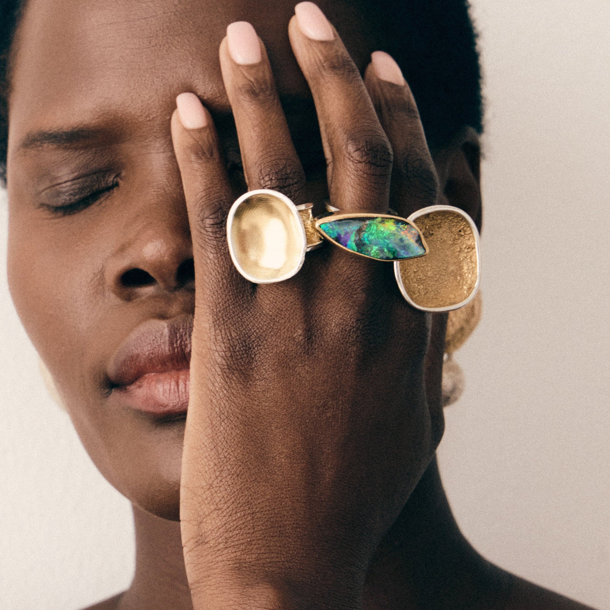 Person wearing a ring with a colorful gemstone on a plain background