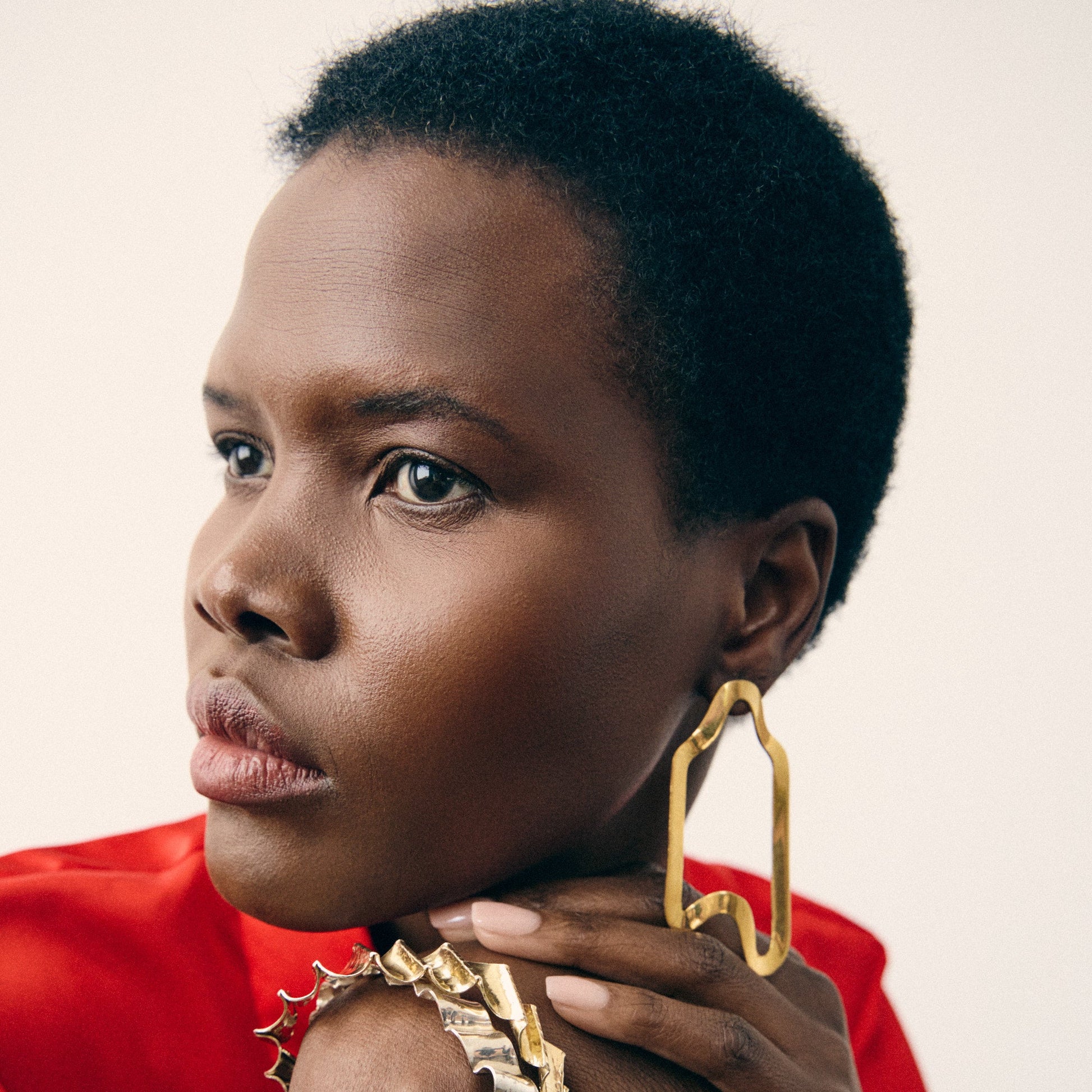 Woman wearing gold hoop earrings and a red top against a neutral background