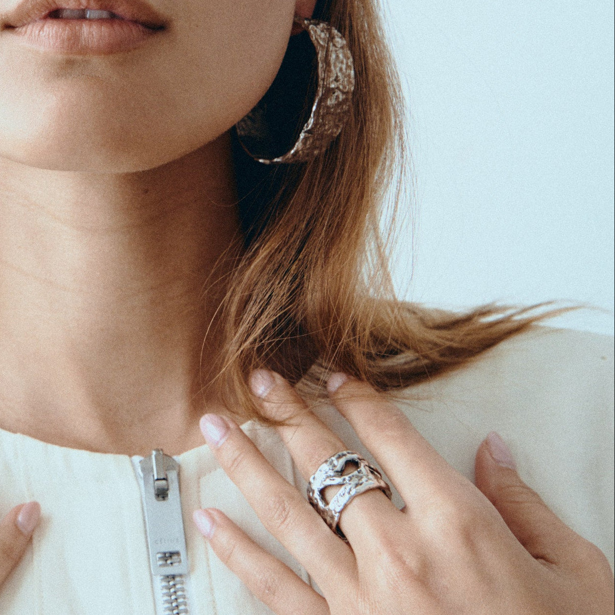Woman wearing multiple rings and hoop earrings against a light blue background