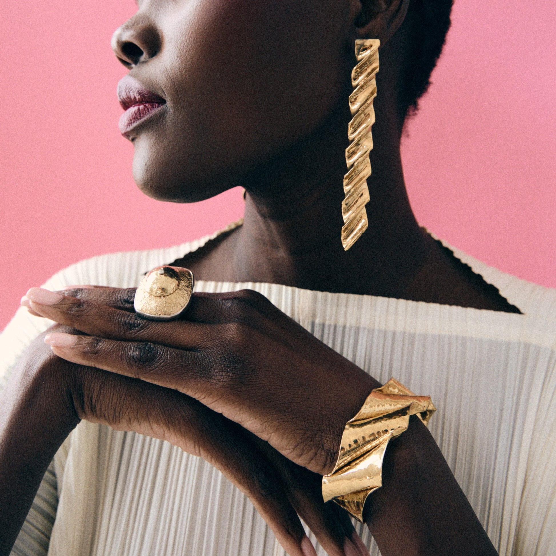 Woman wearing gold jewelry against a pink background