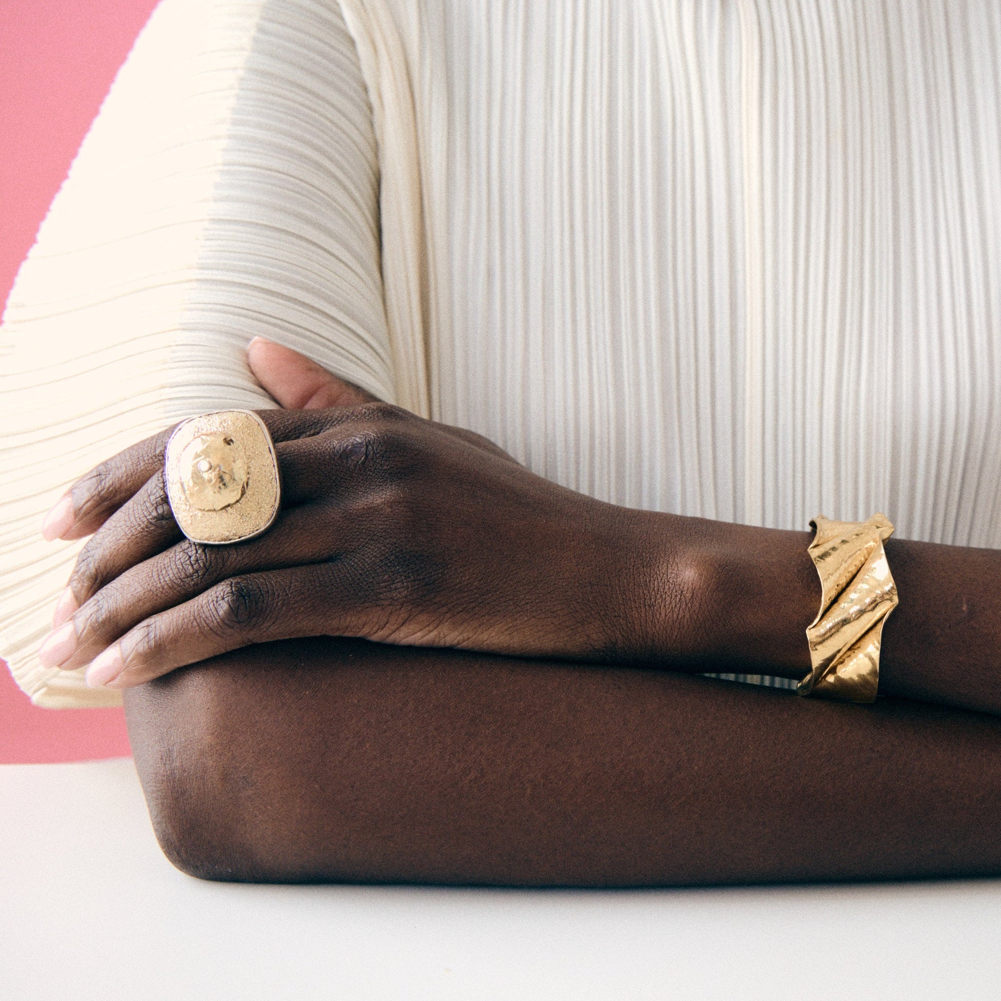 Person wearing gold rings and bracelet on a pink and white background