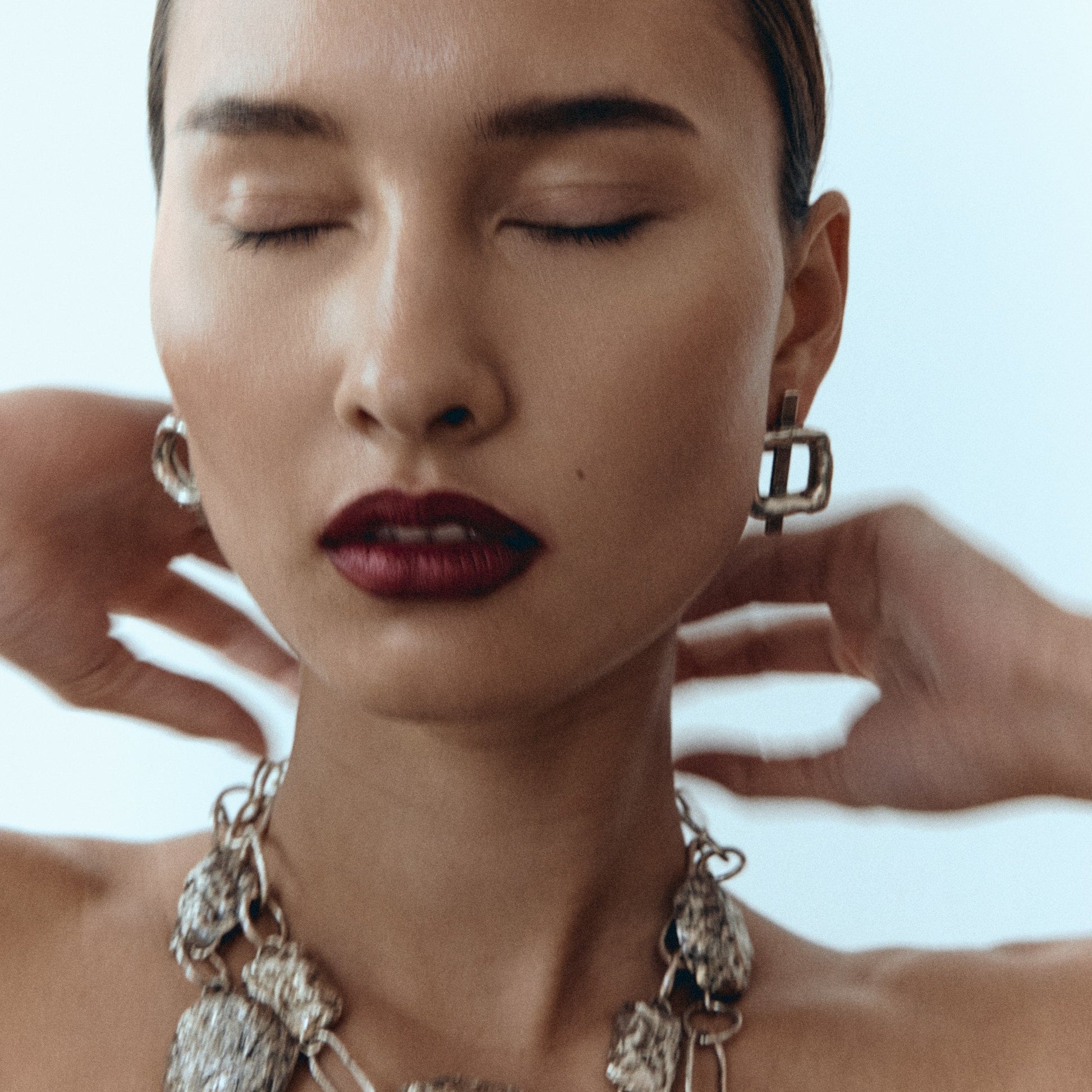 Woman wearing a silver necklace with a plain background