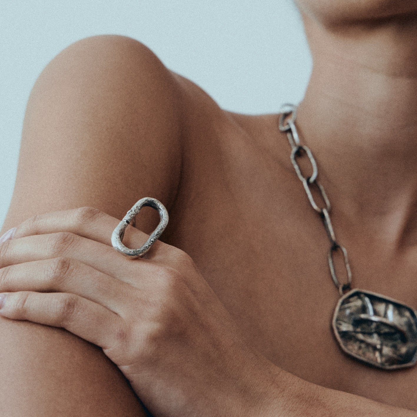 Woman wearing a silver necklace and statement ring against a plain background