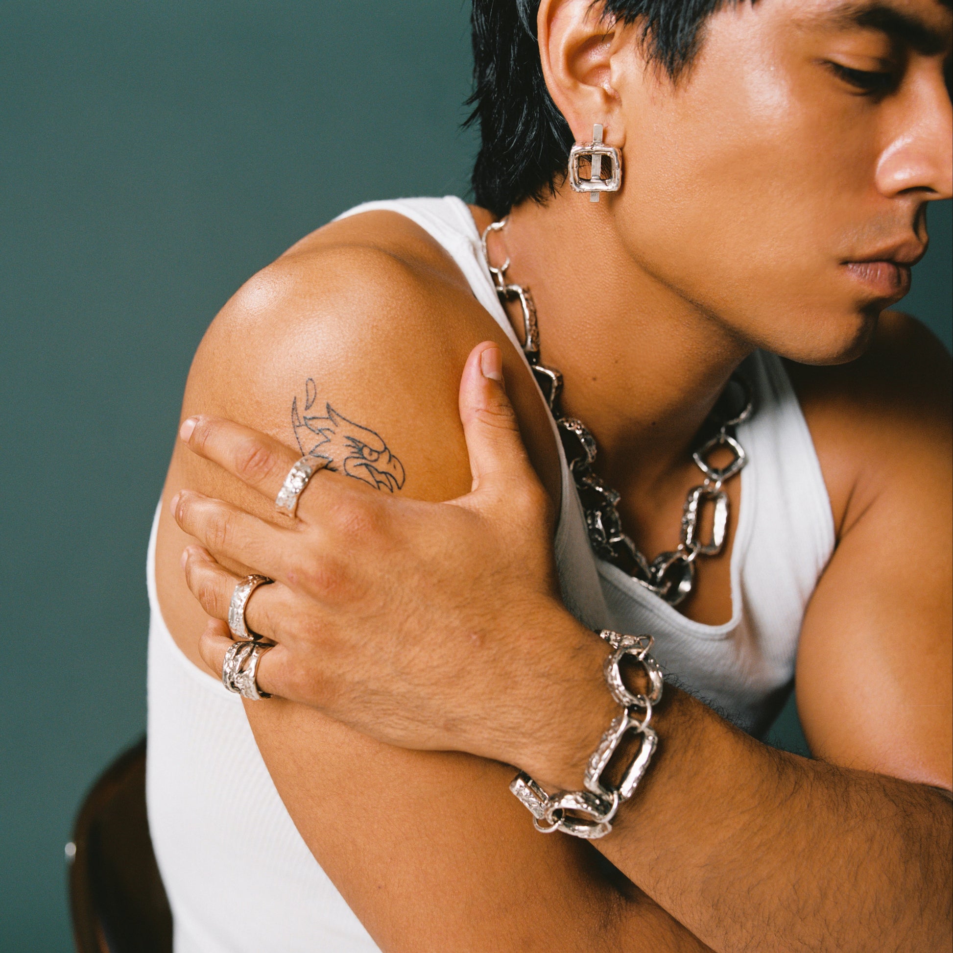 Person wearing silver chain necklace and bracelet with a tattoo on shoulder against a green background