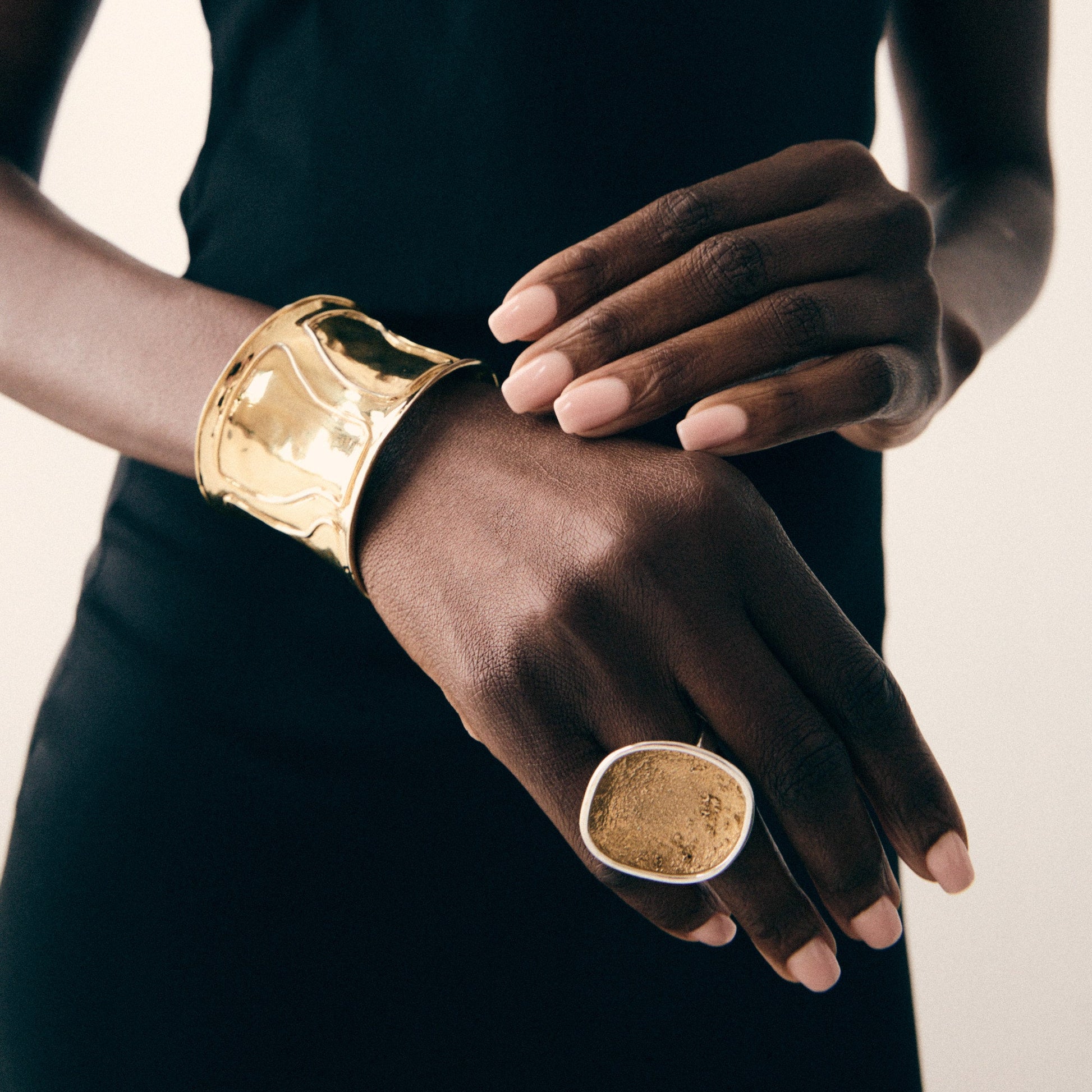 Person wearing a gold bracelet and ring on a plain background