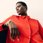 Person wearing a red jacket with gold jewelry on a plain background