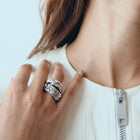 Close-up of a person wearing silver hoop earrings and rings on a light background