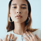 Woman wearing multiple rings and hoop earrings against a light blue background