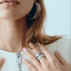 Woman wearing multiple rings and hoop earrings against a light blue background