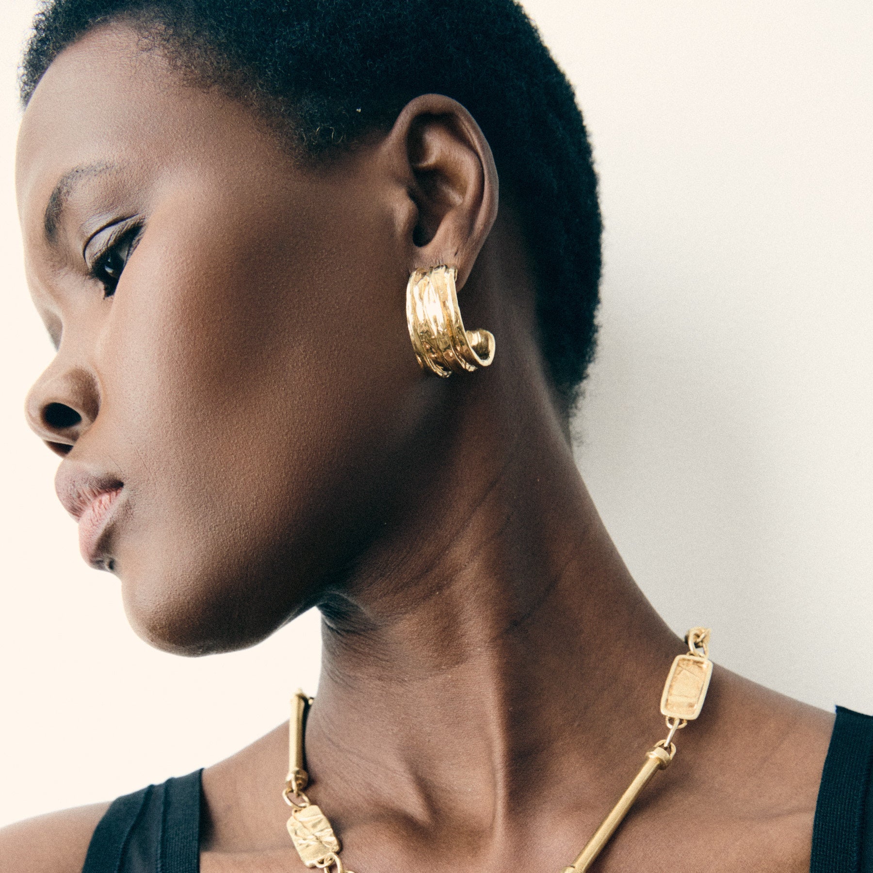 Woman wearing a gold necklace and hoop earrings against a neutral background