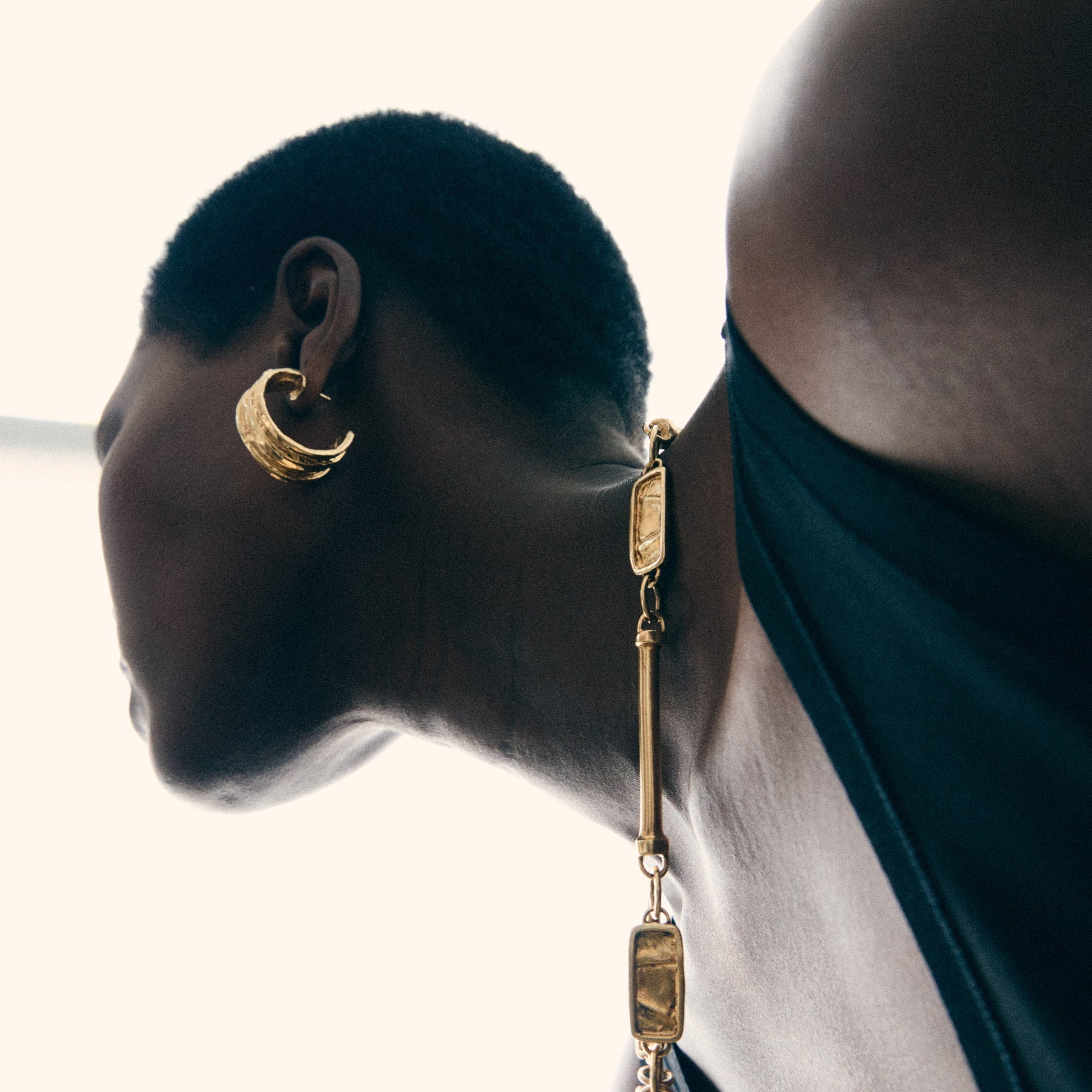 Gold earring with chain detail worn by a person against a neutral background