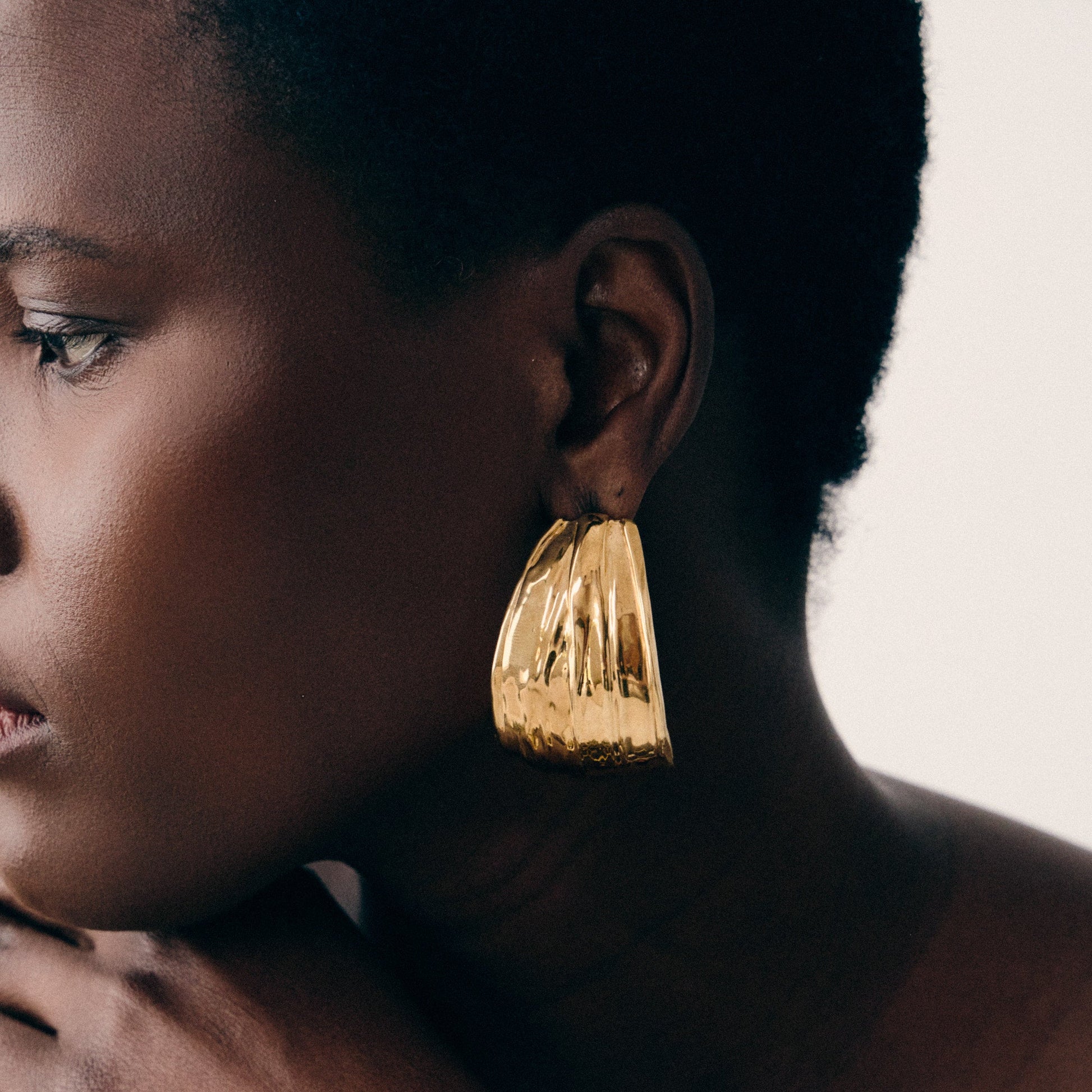 Woman wearing gold earrings and bracelet against a neutral background