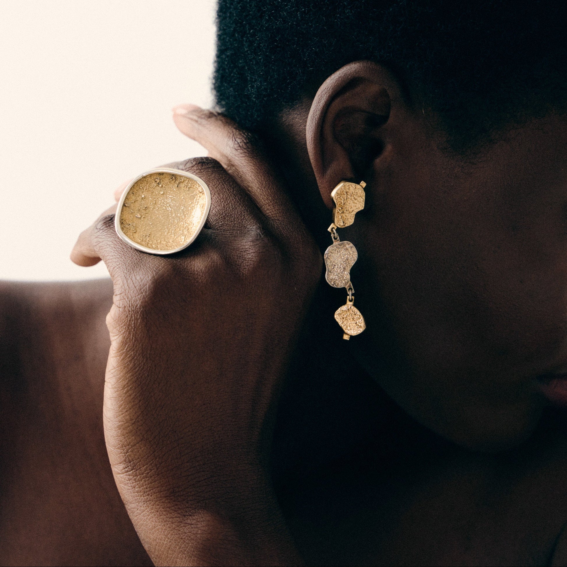 Person wearing gold earrings and a ring, with a neutral background