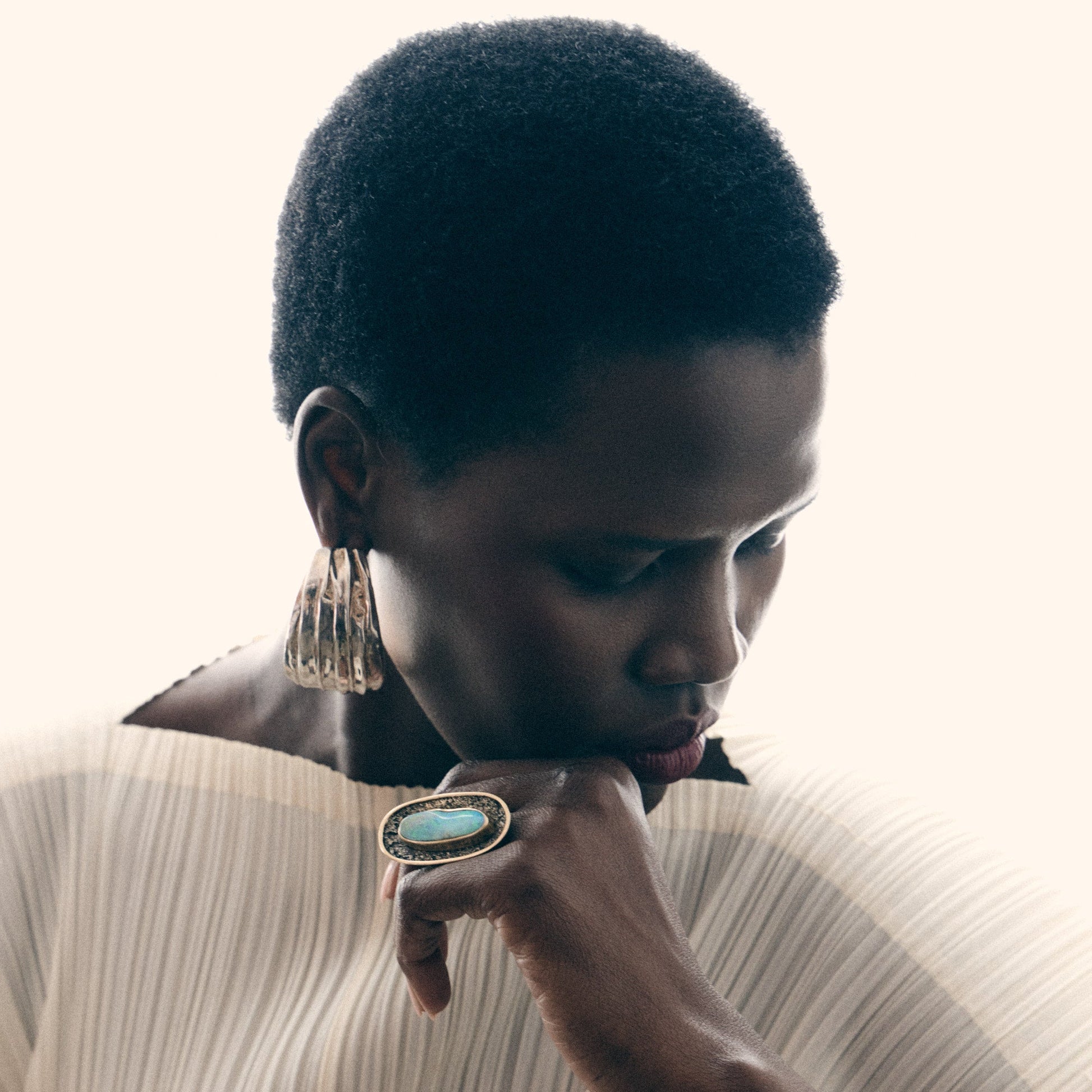 Woman wearing a ring with a large earring, looking down.