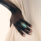 Hand wearing a ring with a turquoise stone on a textured white background