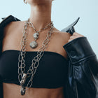 Woman wearing a black top and leather jacket with layered necklaces against a light background