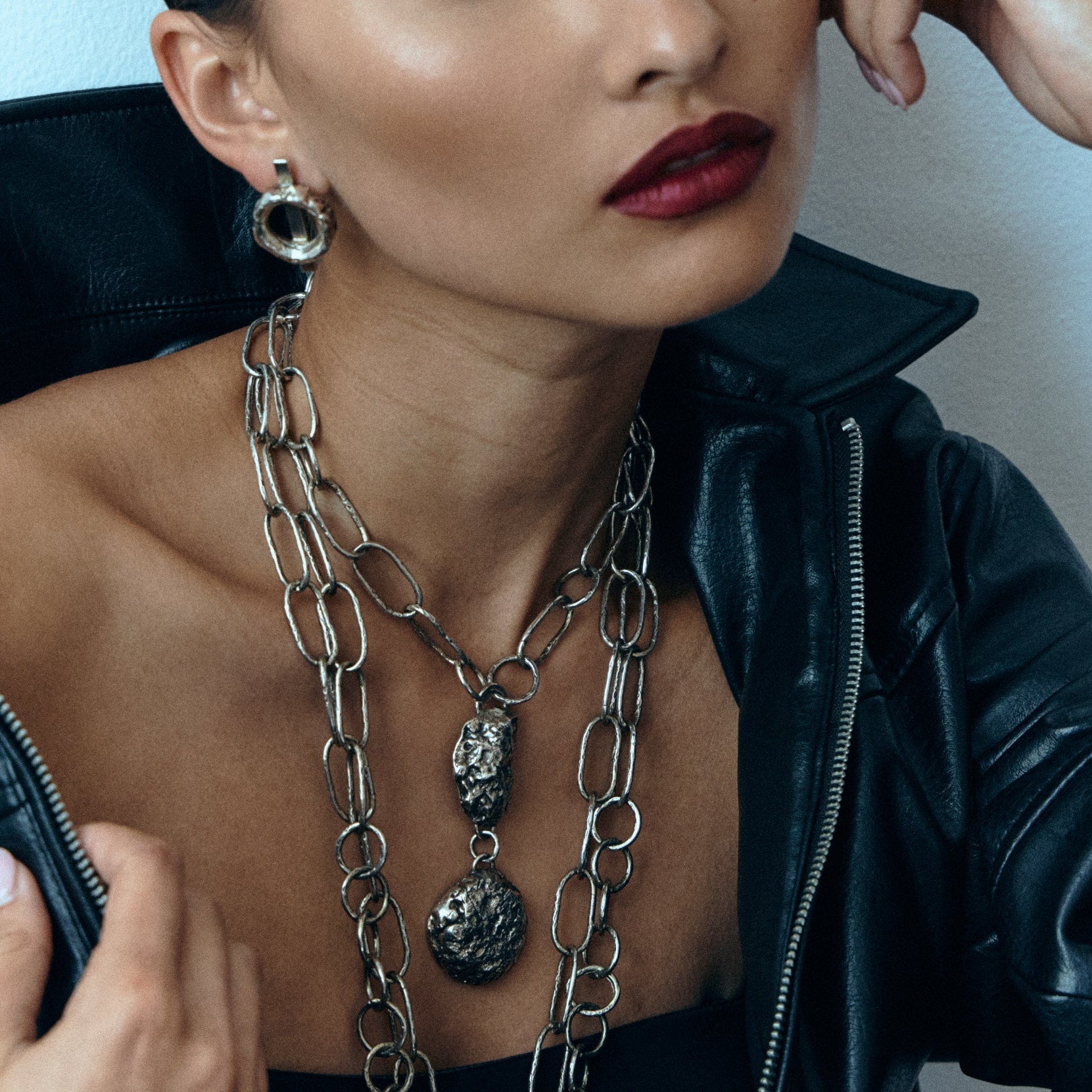 Woman wearing a black leather jacket and layered necklaces against a light background