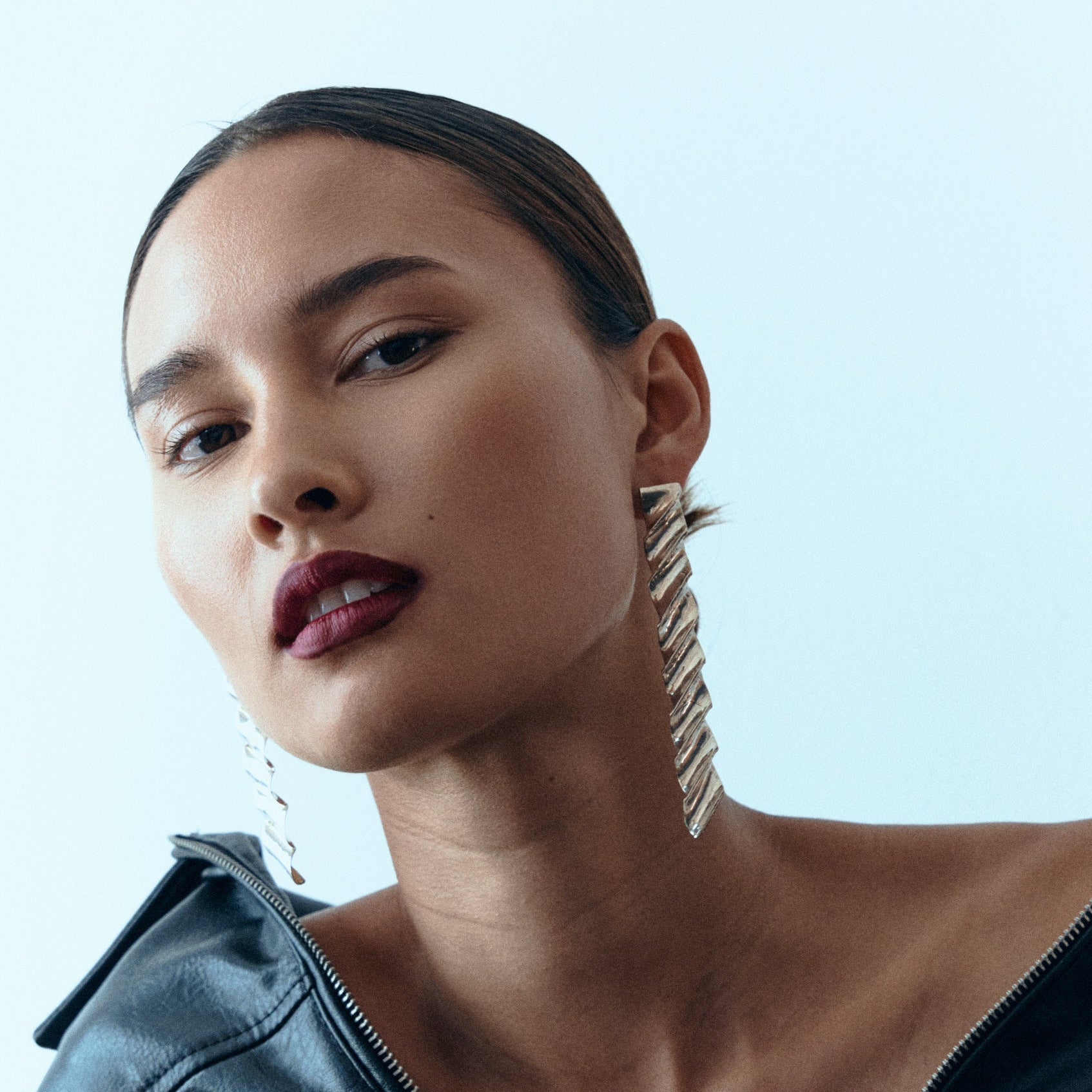 Woman wearing a large diamond ring and hoop earrings against a light blue background