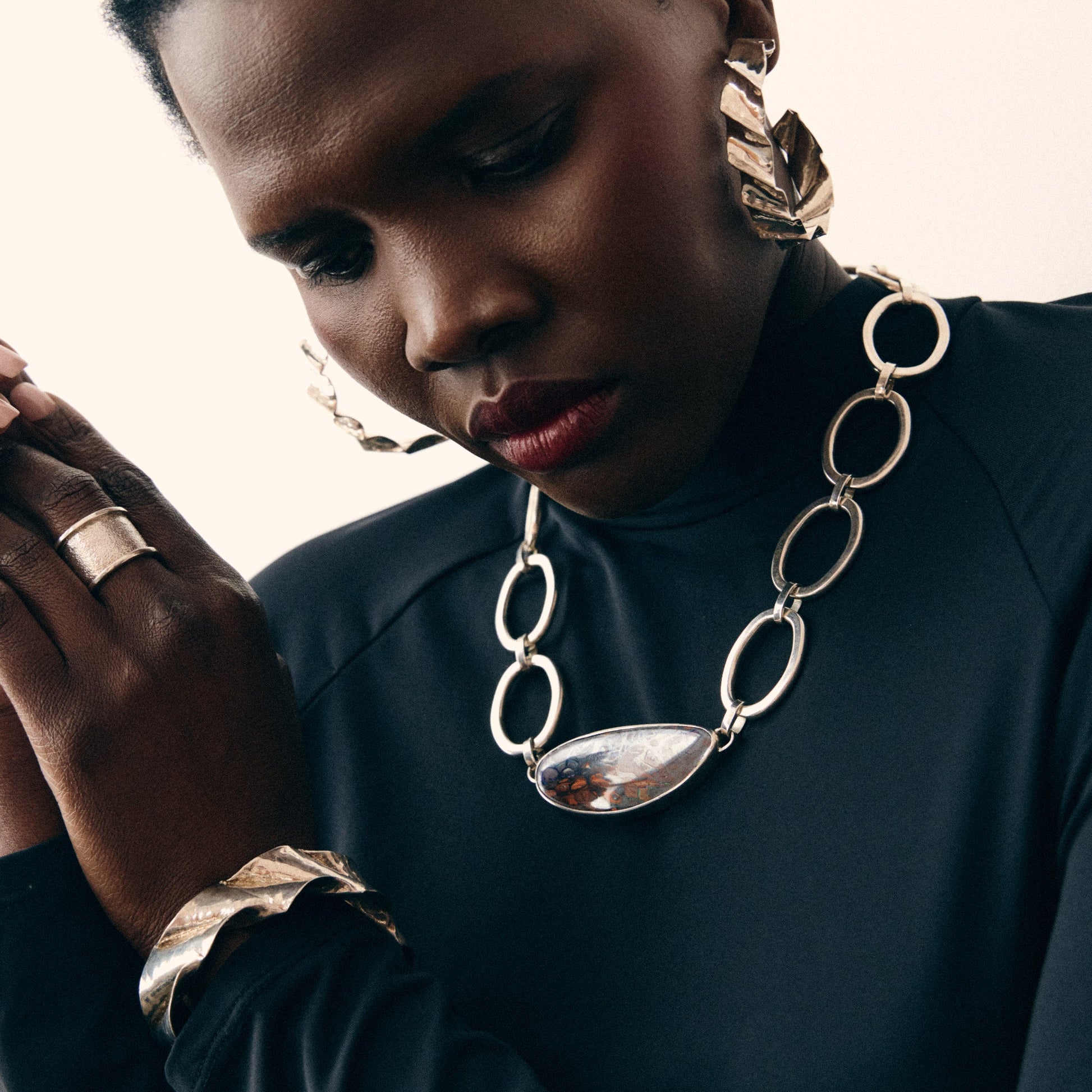 Person wearing a silver chain necklace and ring on a neutral background