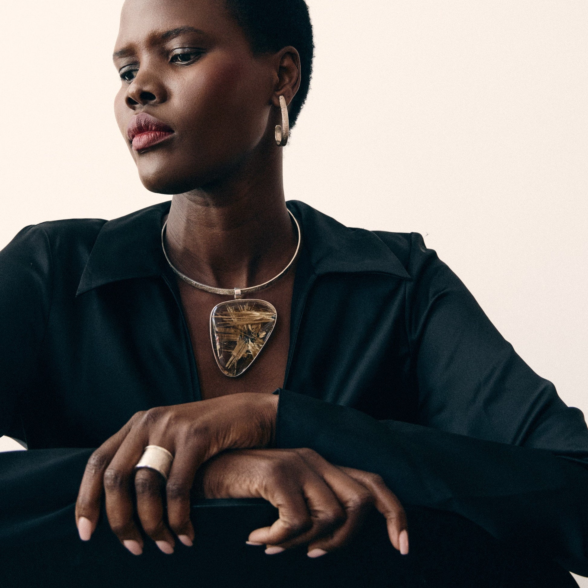 Person wearing a black outfit with a gold necklace against a neutral background