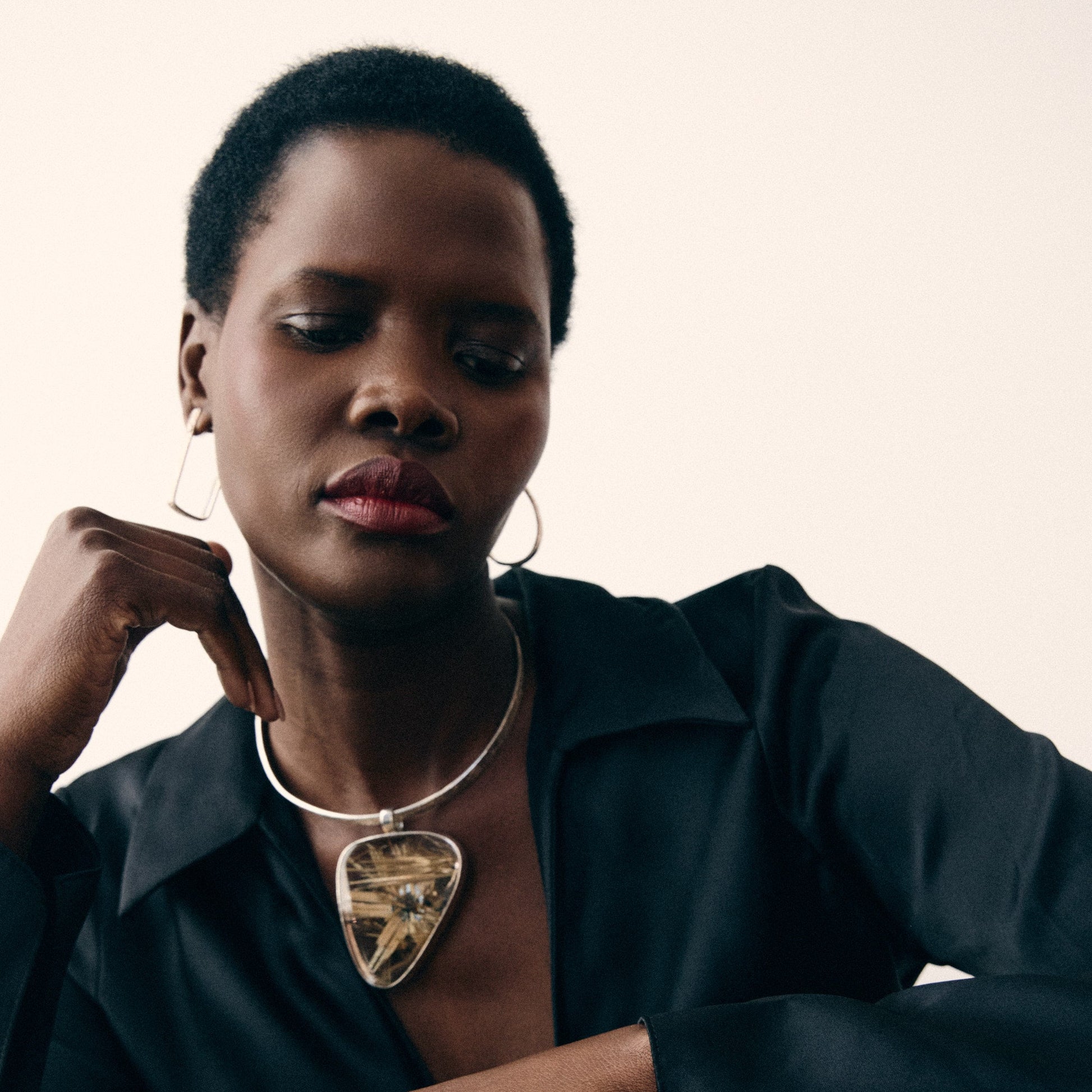 Woman wearing a black outfit with a necklace against a neutral background