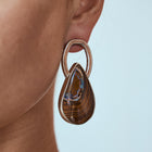 Close-up of a person wearing a pair of teardrop-shaped earrings with a light blue background