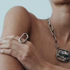 Woman wearing a silver necklace and statement ring against a plain background